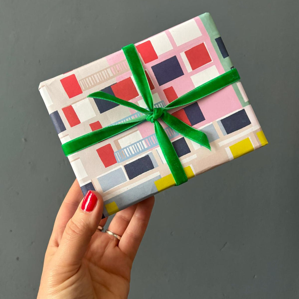 Hand holding a colorful wrapped gift with a green ribbon against a gray background